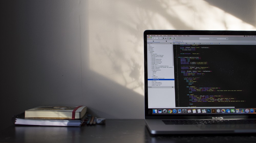 “Two books on a desk near a MacBook with lines of code on its screen” by Émile Perron on Unsplash